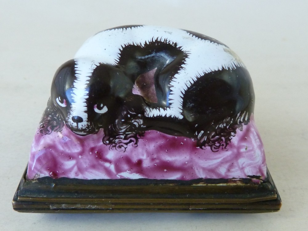 An eighteenth-century Bilston enamel snuff box depicting a black and white King Charles spaniel curled on a magenta cushion base with metal mounts.