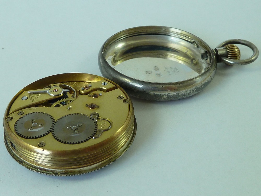 An opened Edwardian silver pocket watch case resting beside its gilt brass mechanical watch movement.