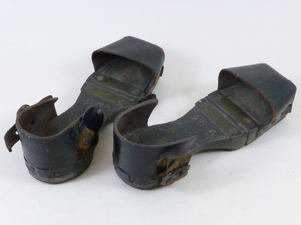 A pair of antique child hinged wooden overshoes featuring dark leather toe caps and heel straps with metal fittings. View II