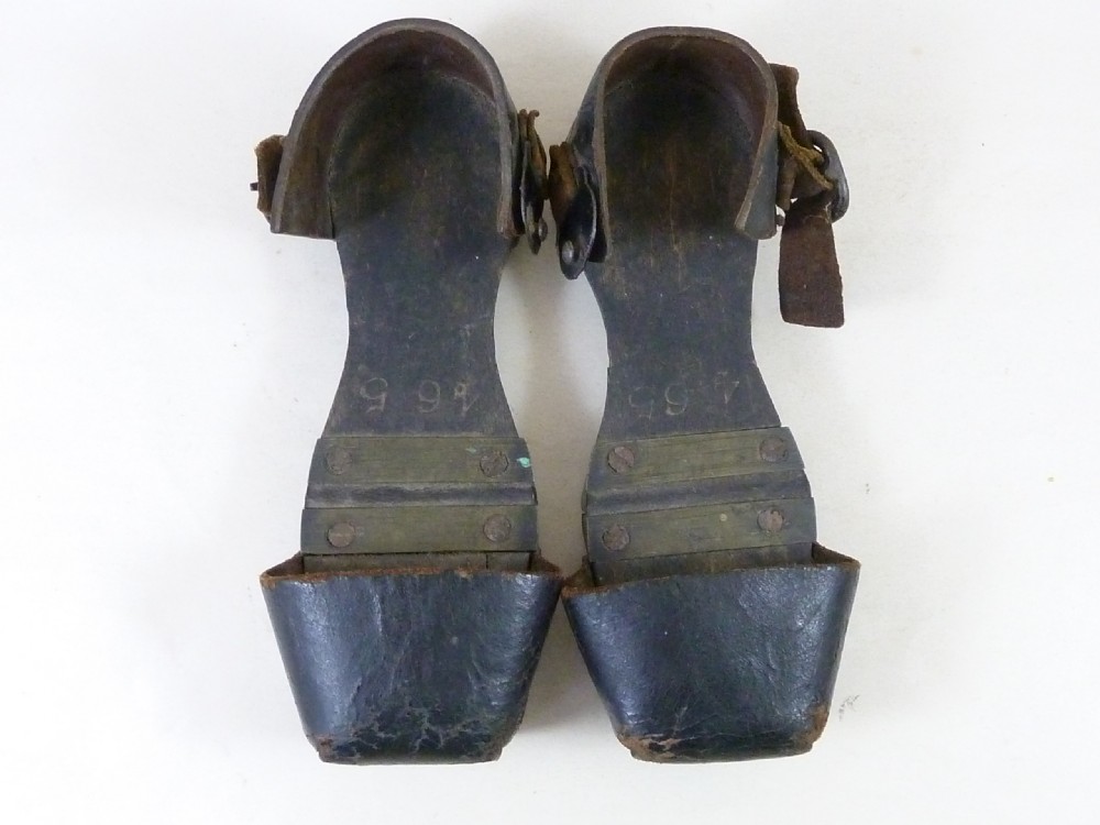 A pair of antique child hinged wooden overshoes featuring dark leather toe caps and heel straps with metal fittings. View III