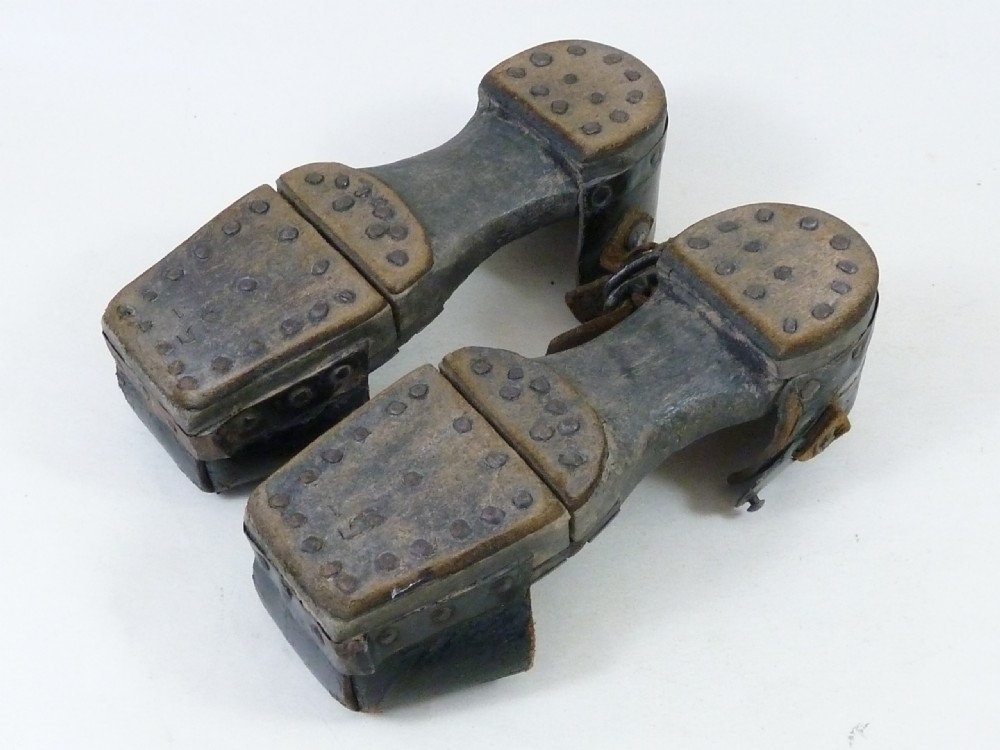 A pair of antique child hinged wooden overshoes featuring dark leather toe caps and heel straps with metal fittings. View IV