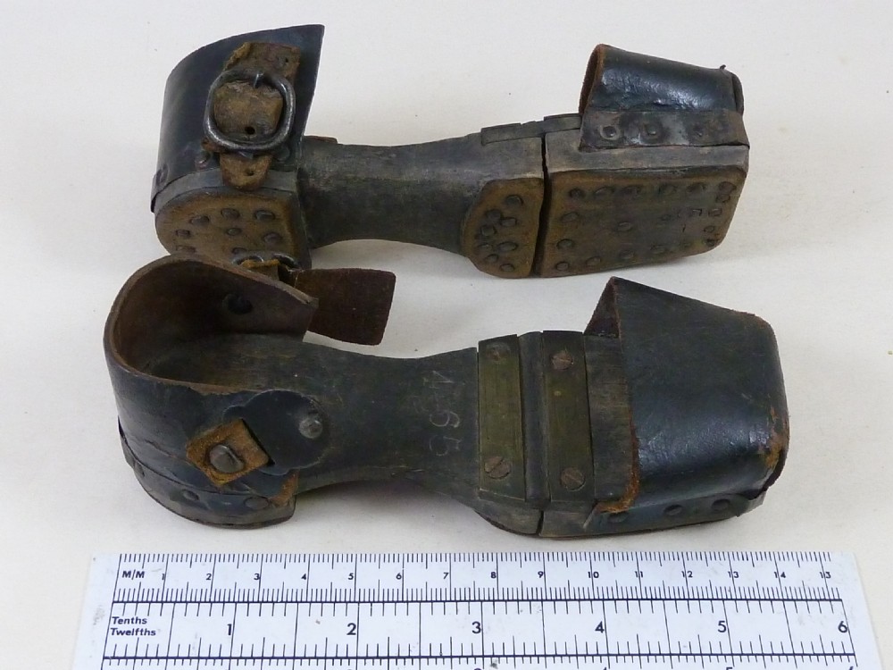 A pair of antique child hinged wooden overshoes featuring dark leather toe caps and heel straps with metal fittings. View VI