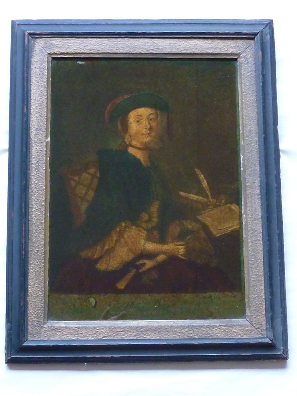 A framed 18th-century reverse glass print depicting a portrait of a seated lady wearing a green cloak and cap next to a desk with a quill.