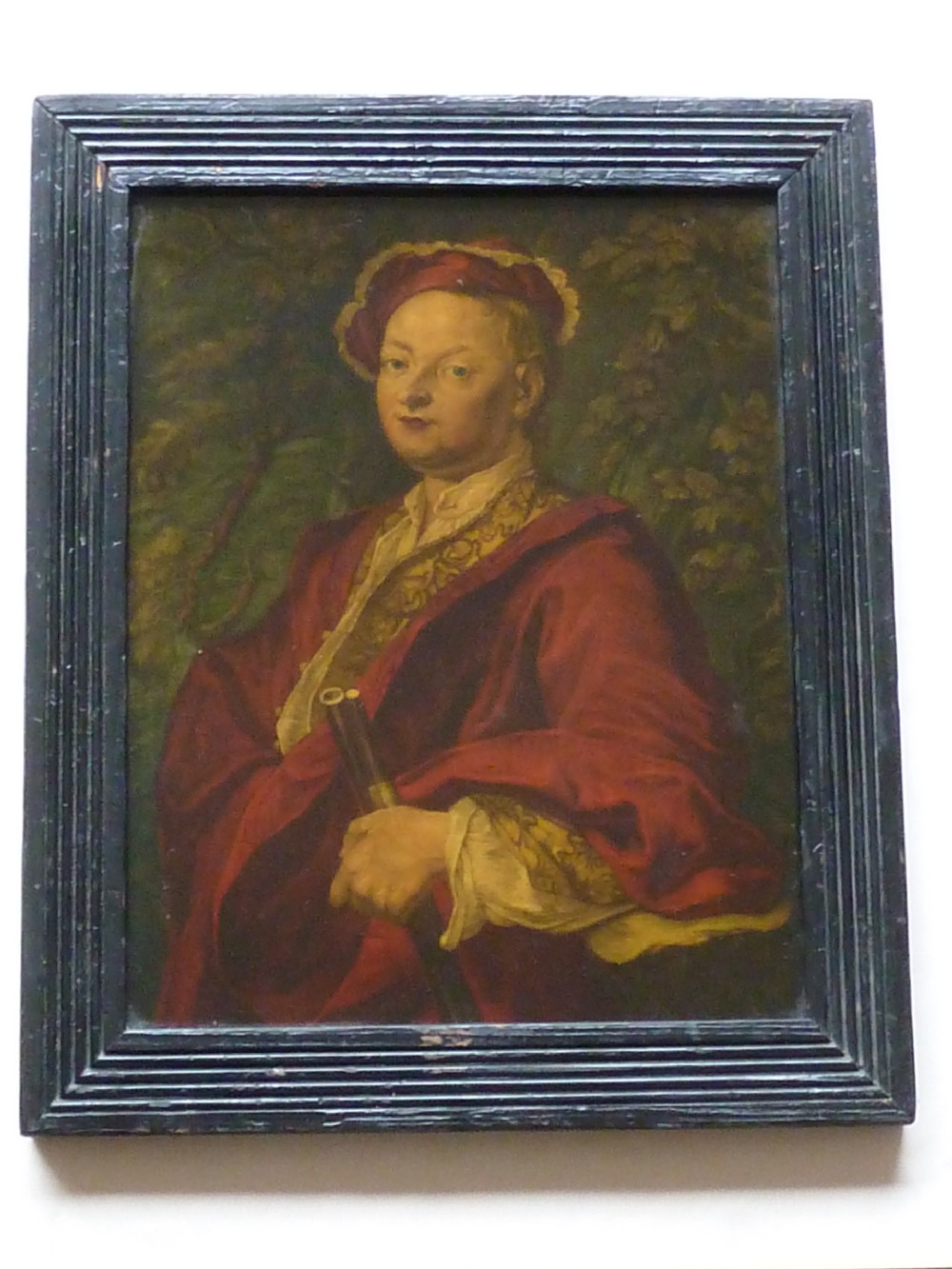 An 18th-century Georgian reverse glass painted portrait featuring a gentleman in a red robe holding a gun barrel within a dark moulded frame.