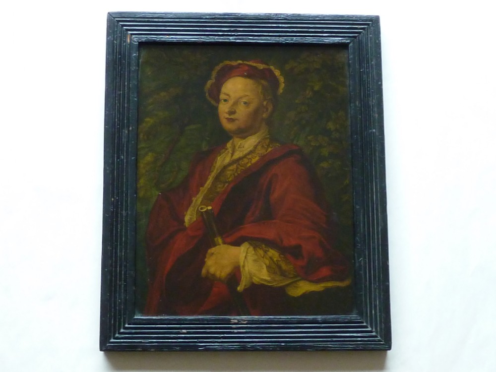 An 18th-century Georgian reverse glass painted portrait featuring a gentleman in a red robe holding a gun barrel within a dark moulded frame. View II