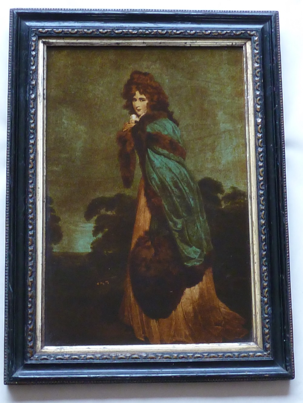 A Georgian reverse glass painted print depicting Elizabeth Farren wearing a green fur-trimmed cloak, set in a dark moulded wooden frame with a gilt inner border.
