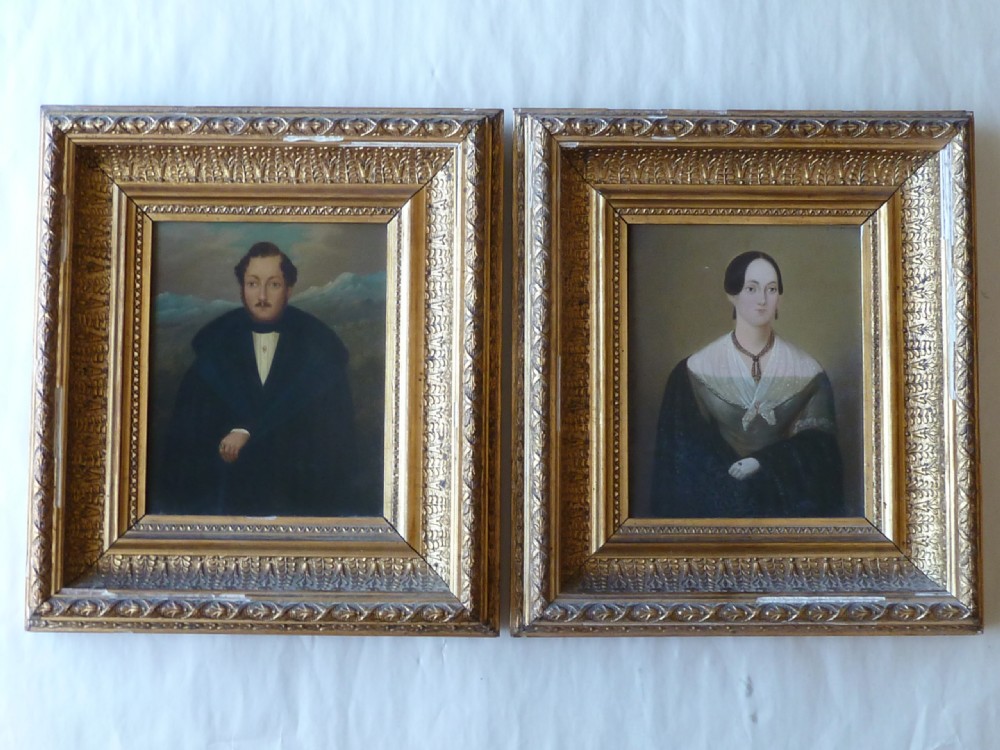 A pair of 19th-century naive portrait paintings on tinplate depicting a man and a woman, framed in heavy carved gilt frames.
