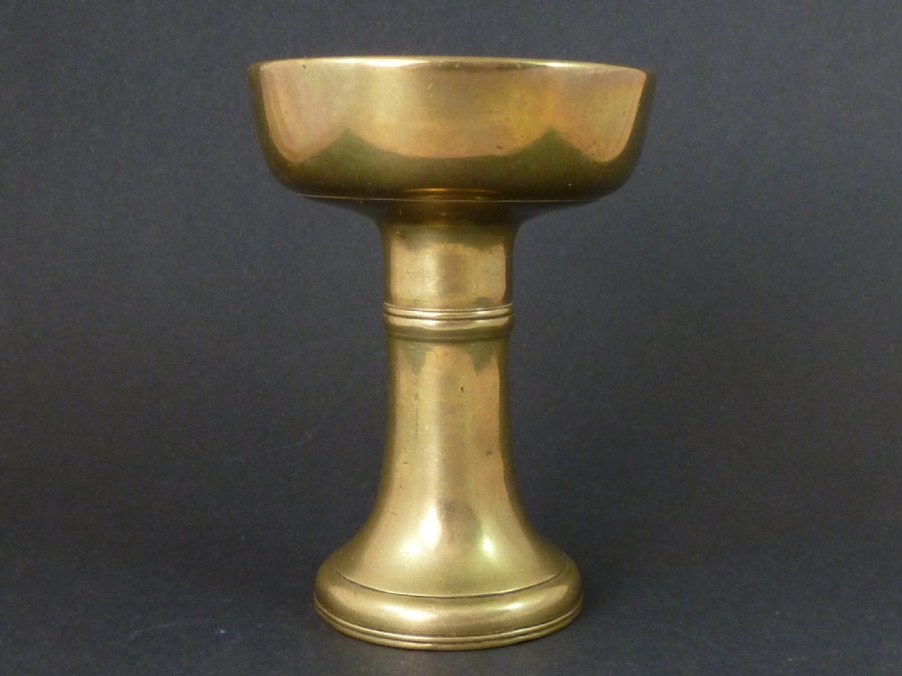 A solid brass Tibetan butter lamp displaying a flared circular base, knopped stem, and wide shallow rimmed upper bowl.