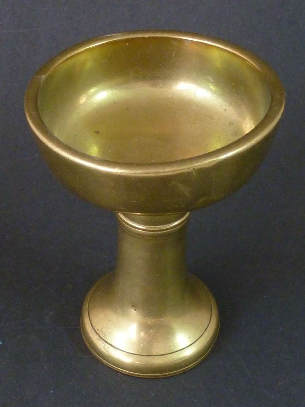 A solid brass Tibetan butter lamp displaying a flared circular base, knopped stem, and wide shallow rimmed upper bowl. View IV