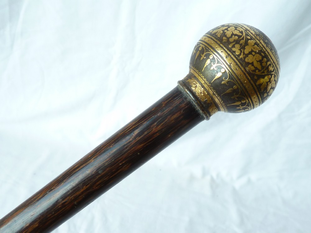 An antique walking stick featuring a round steel ball handle with intricate gold damascene inlay mounted on a dark palm wood shaft. View V