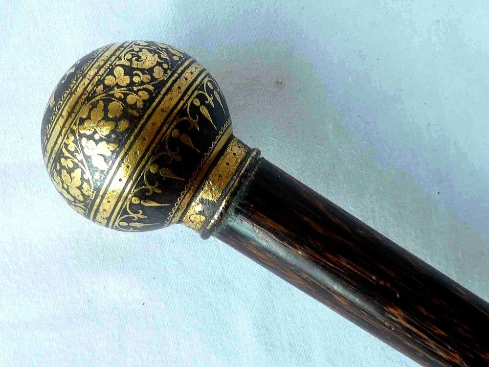 An antique walking stick featuring a round steel ball handle with intricate gold damascene inlay mounted on a dark palm wood shaft.