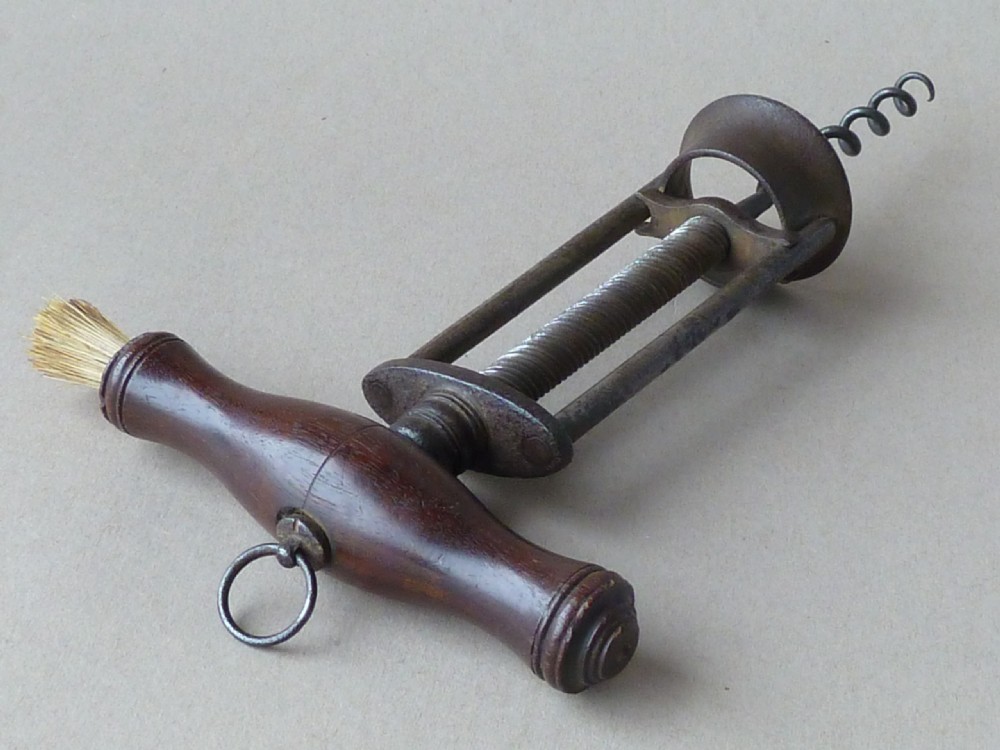 An antique English steel two-pillar corkscrew featuring a central threaded shaft, wire helix, and a turned dark rosewood handle fitted with a small dusting brush. View V