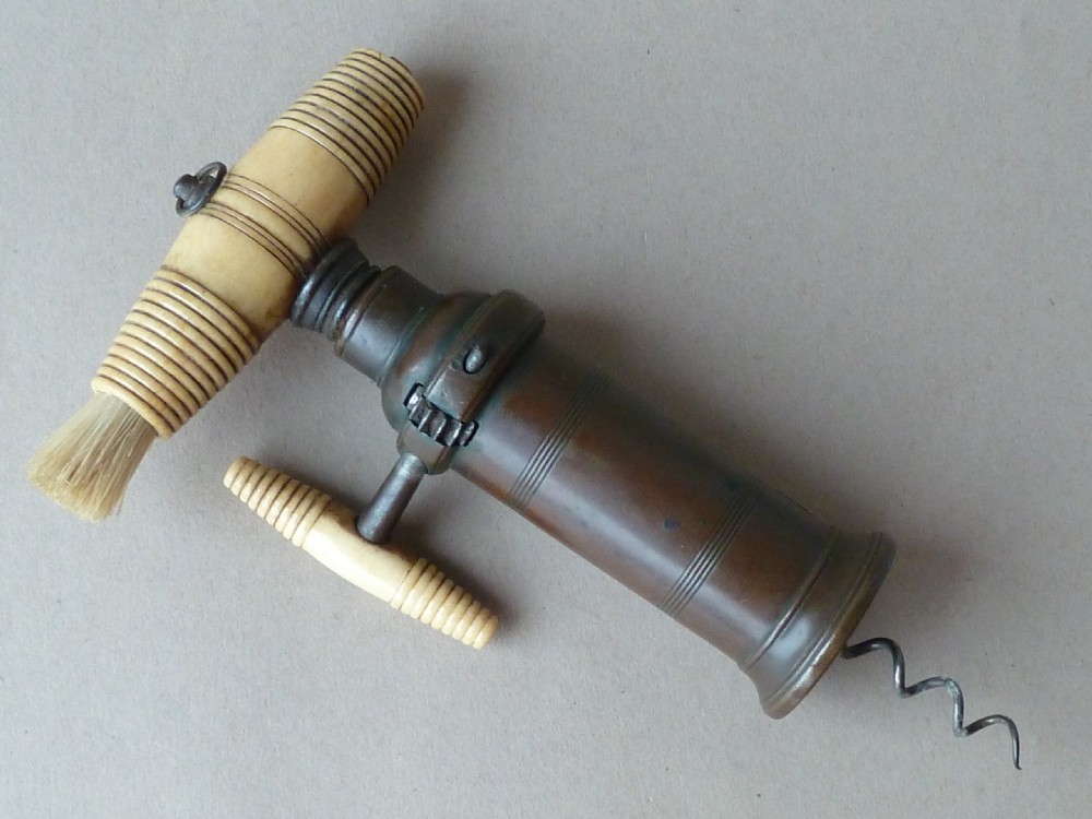 An antique dark bronze Thomason patent corkscrew featuring a turned bone handle, side key, detachable bristle brush, and an applied brass crest. View II