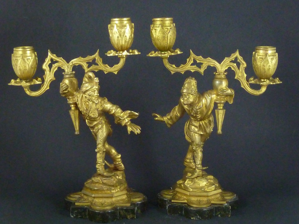 A pair of gilt bronze twin-light figural candelabra featuring sculpted Renaissance figures supporting branching candle arms set upon dark marble bases.