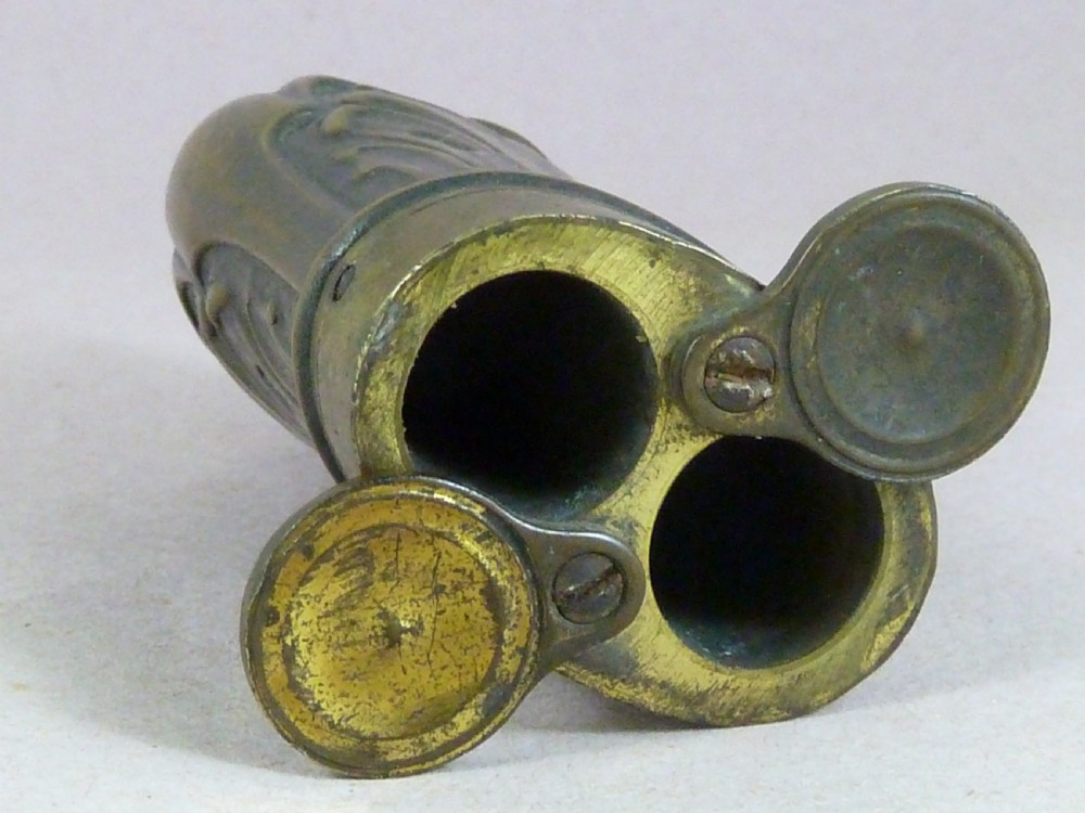 An antique embossed copper and brass three-way pistol flask featuring a central palmette design and a top dispensing nozzle. View VII