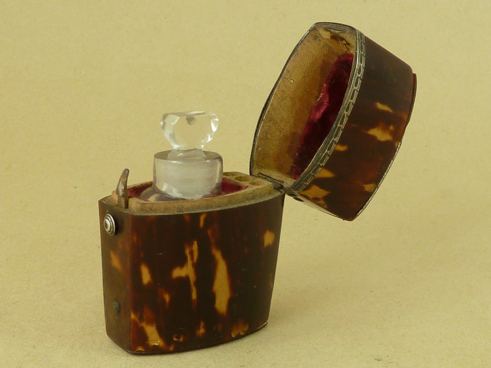 An opened Georgian tortoiseshell etui case lined with red velvet, containing a small clear glass perfume bottle with a faceted stopper.