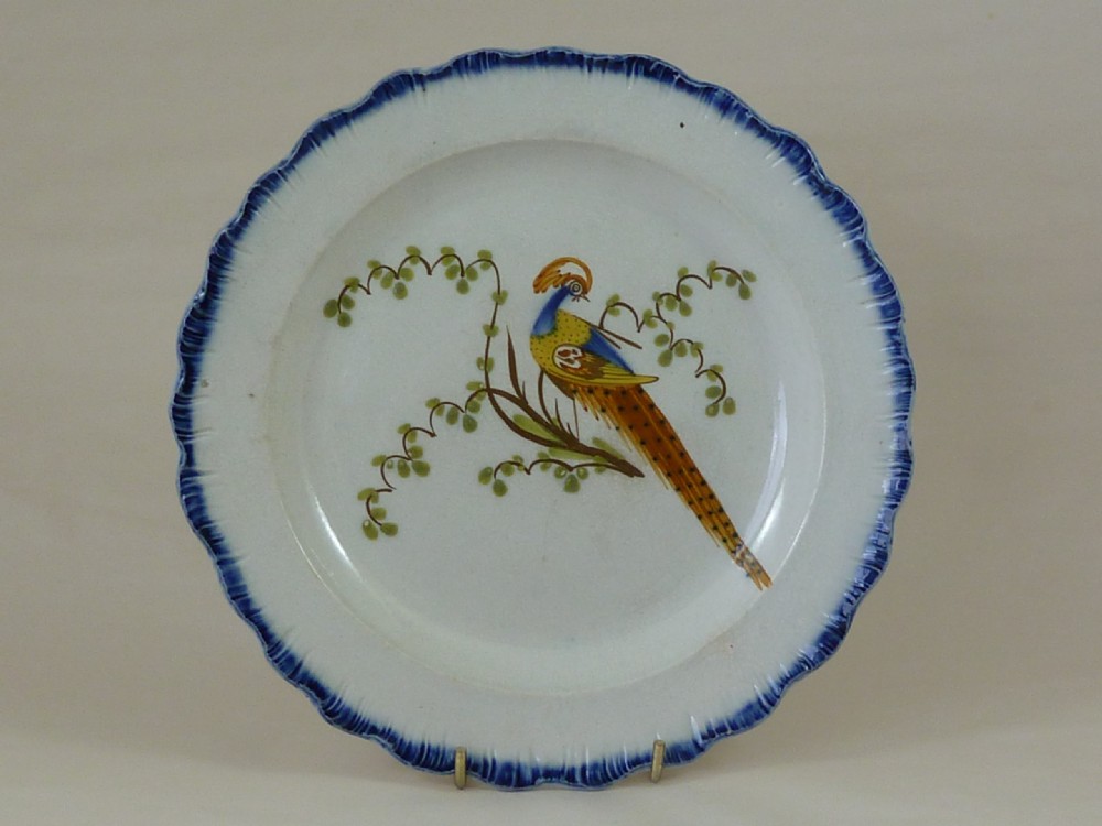 An antique pearlware plate featuring a hand-painted peafowl on a branch framed by a blue feather-edge rim.
