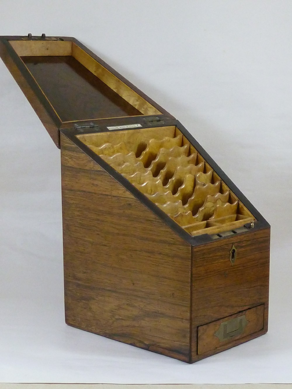A Victorian rosewood sloping desktop stationery cabinet with open hinged lid revealing tiered light-wood compartments and a lower drawer with brass handle.