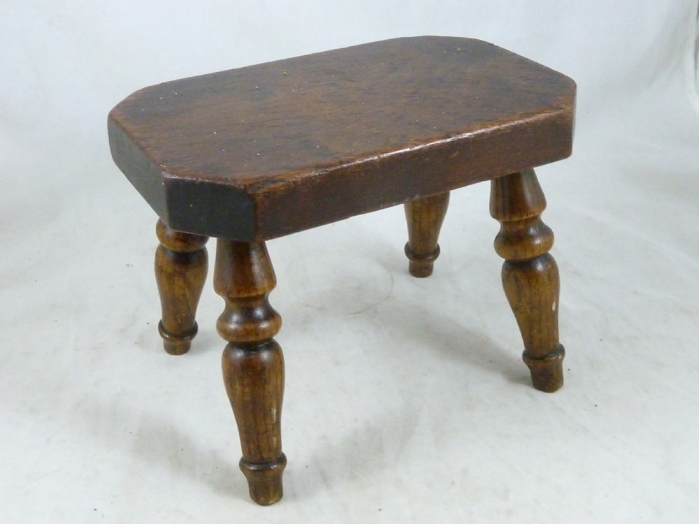 A small antique dark wooden stool featuring a rectangular top and four turned baluster legs. View VI