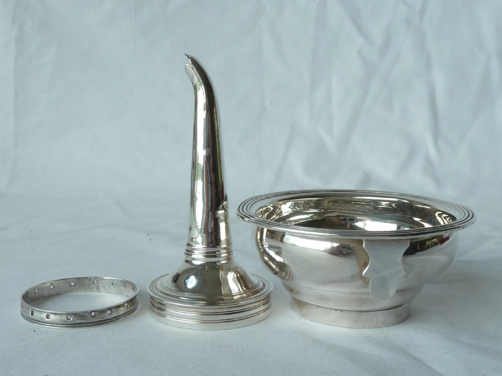 A Georgian sterling silver three-piece wine funnel shown disassembled into a pierced ring, curved spout base, and silver bowl.