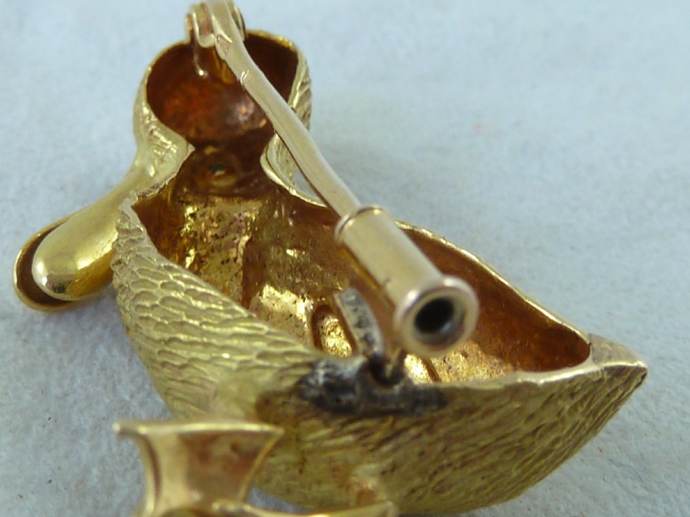 An 18ct yellow gold brooch designed as a standing duckling with textured feathers, an open bill, webbed feet, and a green emerald eye. View IV
