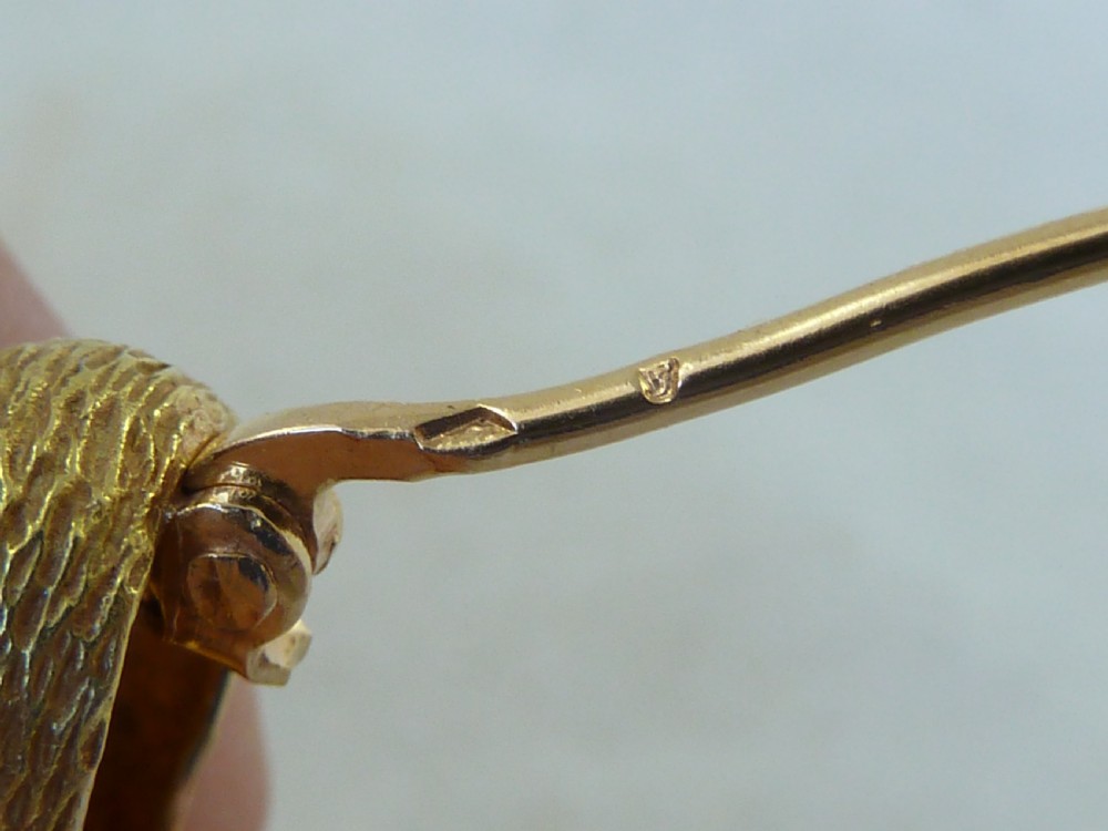 An 18ct yellow gold brooch designed as a standing duckling with textured feathers, an open bill, webbed feet, and a green emerald eye. View VI