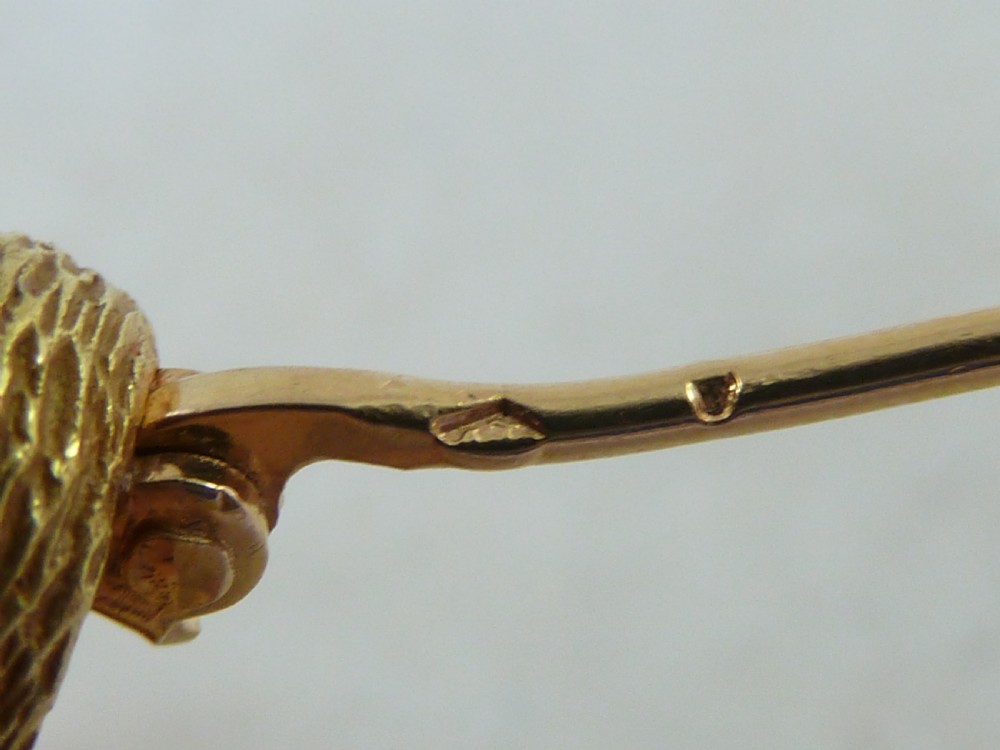 An 18ct yellow gold brooch designed as a standing duckling with textured feathers, an open bill, webbed feet, and a green emerald eye. View VII