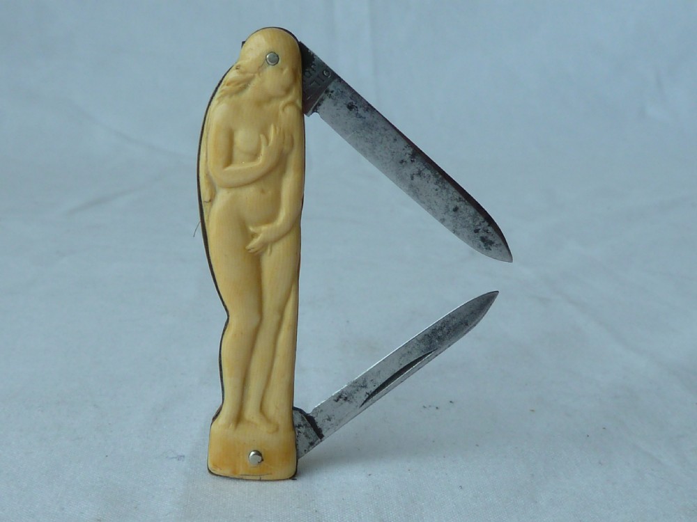 A cream ivorine folding pocket knife moulded in the shape of a female nude figure with two partially opened steel blades.