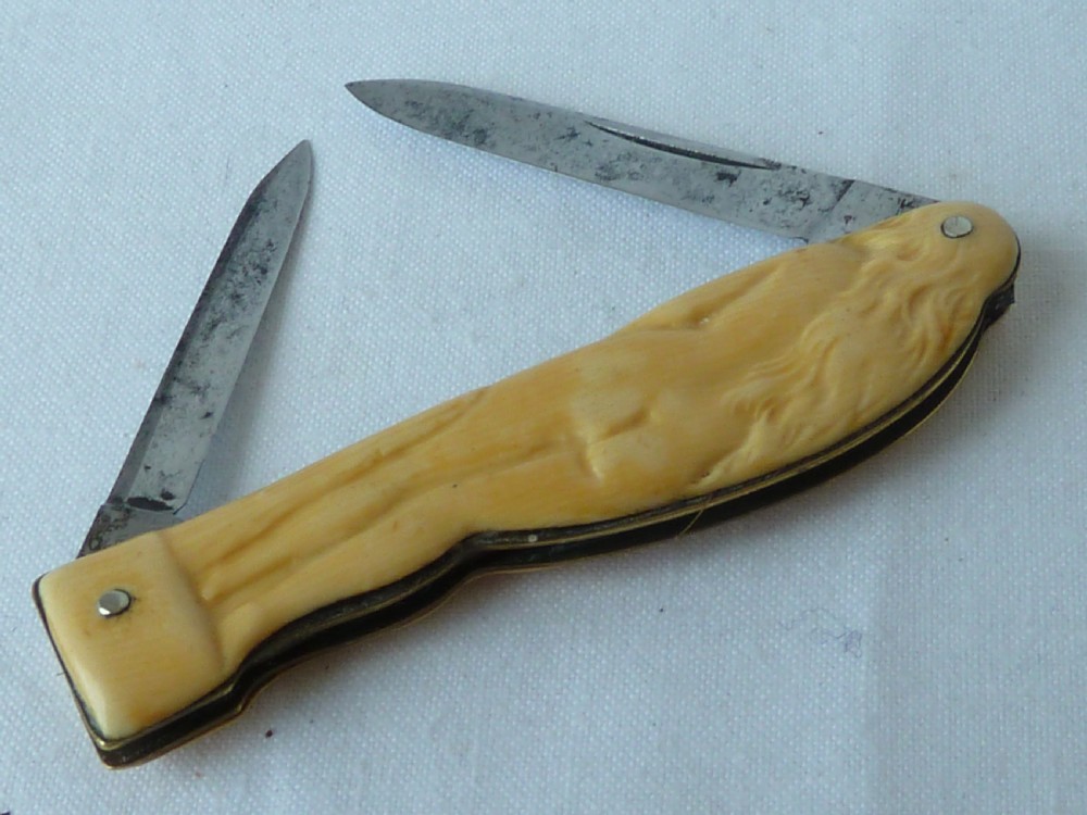 A cream ivorine folding pocket knife moulded in the shape of a female nude figure with two partially opened steel blades. View II
