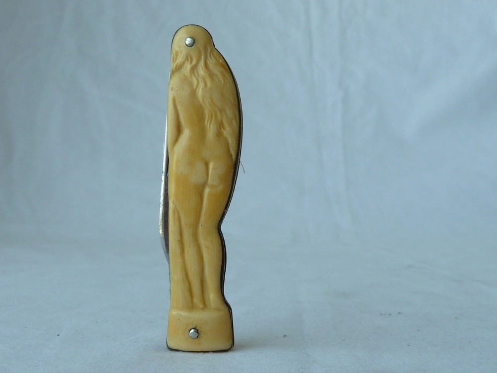 A cream ivorine folding pocket knife moulded in the shape of a female nude figure with two partially opened steel blades. View VII