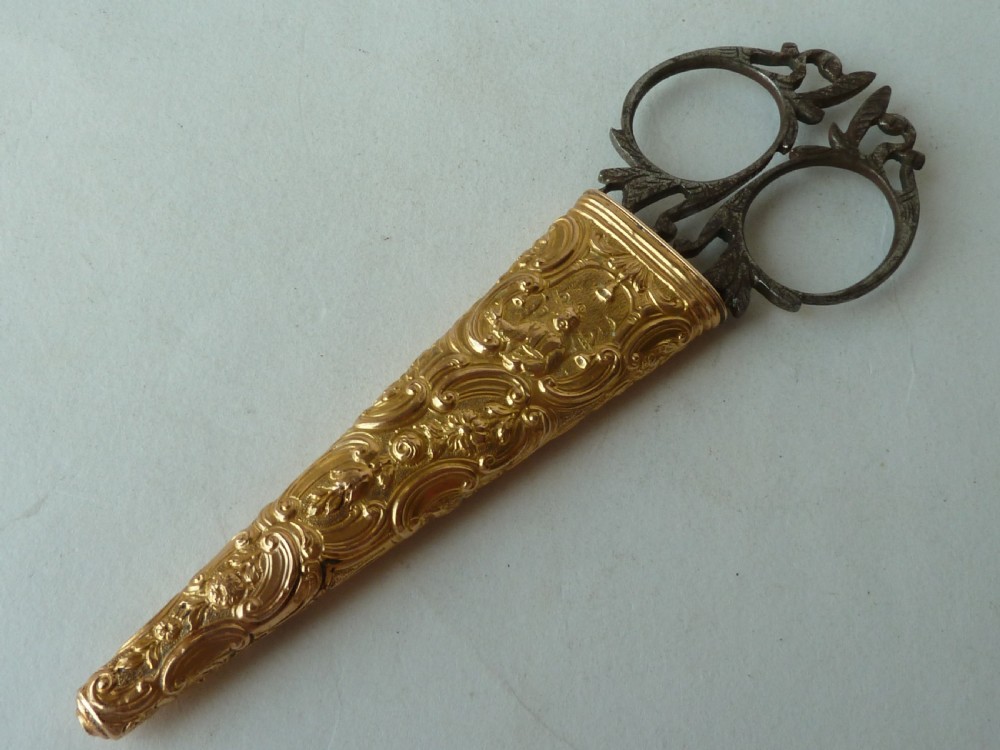 An 18th-century style tapered gold-coloured metal sheath embossed with intricate scrollwork, containing cut steel embroidery scissors. View II