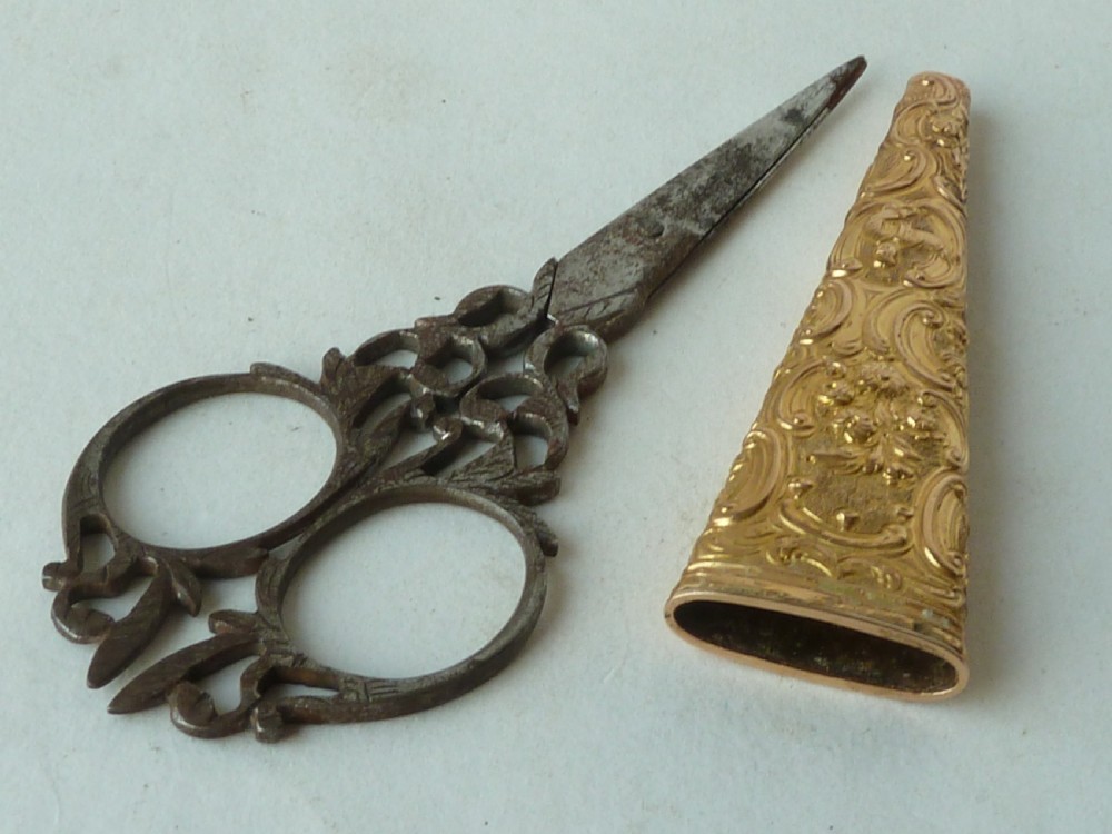 An 18th-century style tapered gold-coloured metal sheath embossed with intricate scrollwork, containing cut steel embroidery scissors. View V