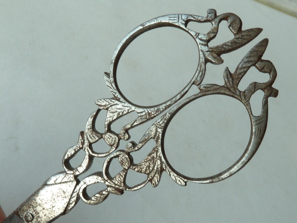 An 18th-century style tapered gold-coloured metal sheath embossed with intricate scrollwork, containing cut steel embroidery scissors. View VI