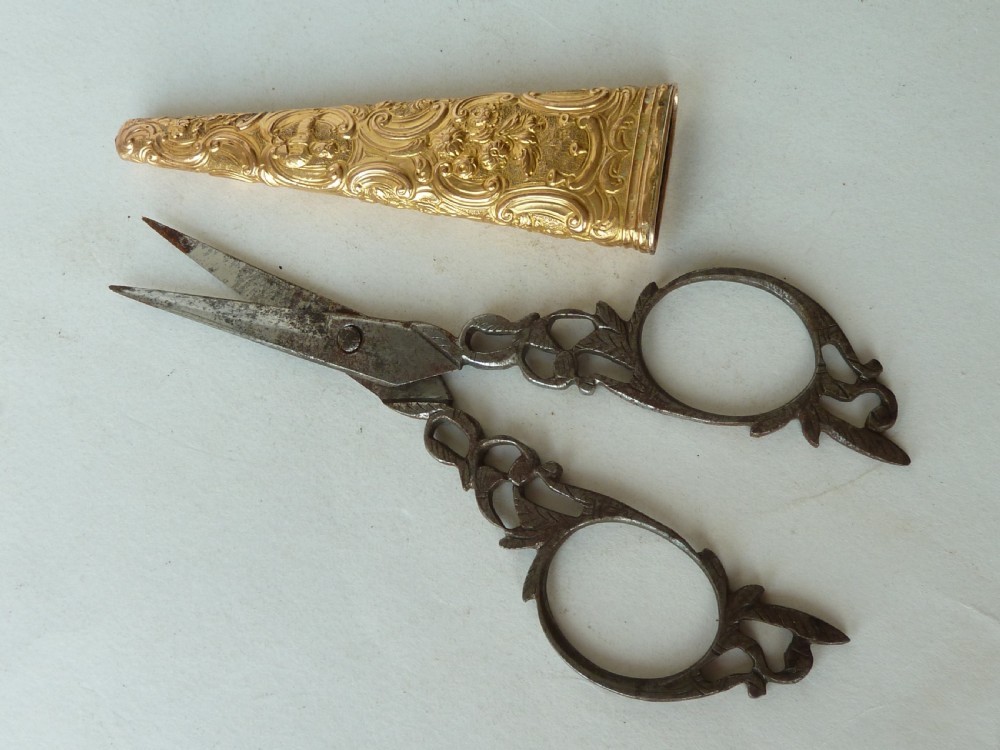 An 18th-century style tapered gold-coloured metal sheath embossed with intricate scrollwork, containing cut steel embroidery scissors. View VII
