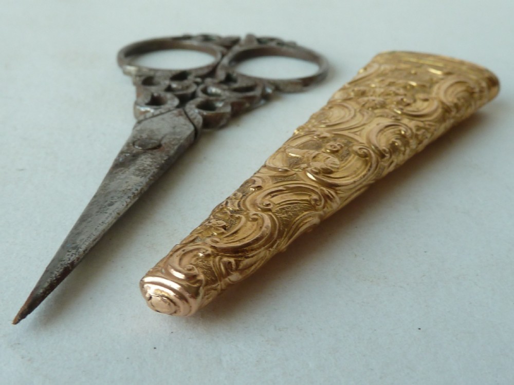 An 18th-century style tapered gold-coloured metal sheath embossed with intricate scrollwork, containing cut steel embroidery scissors. View VIII