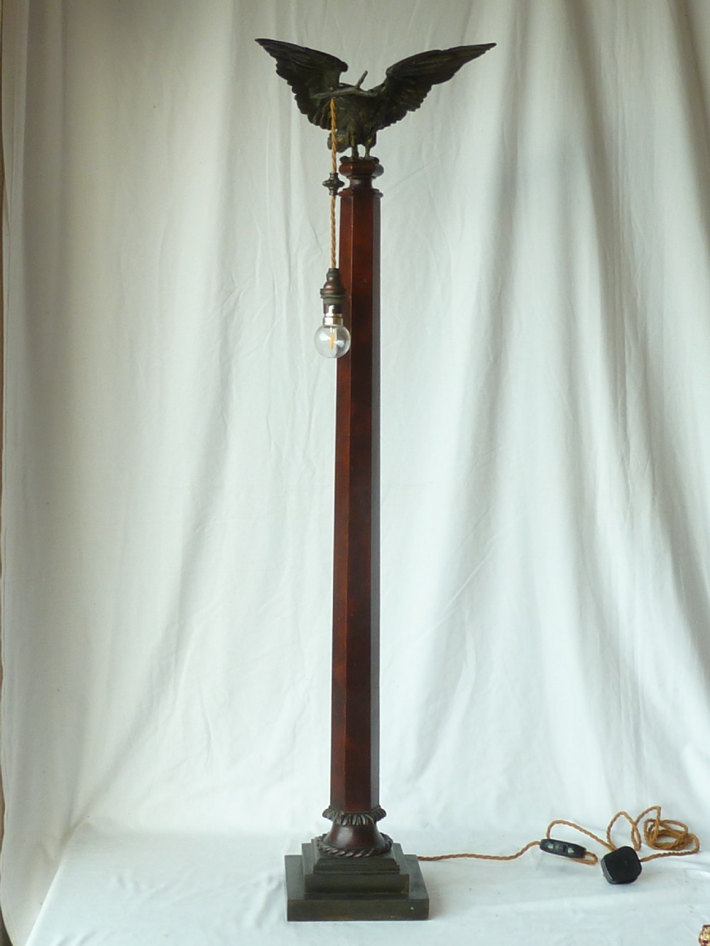 A tall mahogany column table lamp featuring a cast bronze eagle perched at the top above a stepped square plinth base.