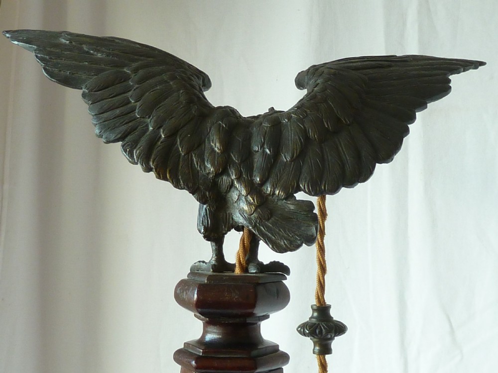 A tall mahogany column table lamp featuring a cast bronze eagle perched at the top above a stepped square plinth base. View X
