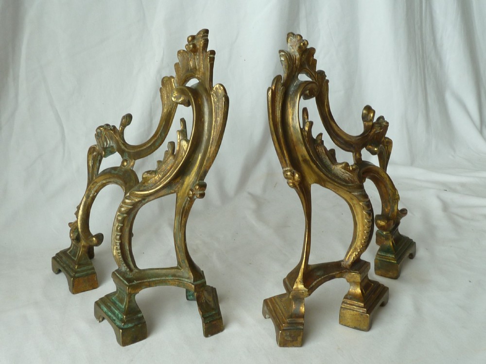 A pair of cast gilt brass French Rococo style fire dogs with elaborate acanthus leaf C-scroll design on small pedestal feet. View II