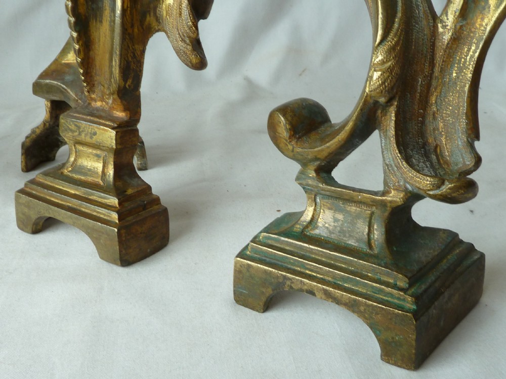 A pair of cast gilt brass French Rococo style fire dogs with elaborate acanthus leaf C-scroll design on small pedestal feet. View V