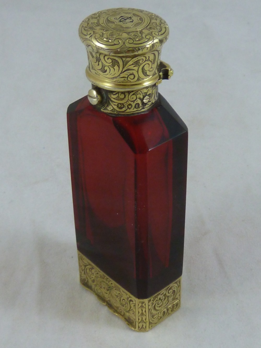 A faceted rectangular ruby red glass scent bottle featuring intricate scroll-engraved silver-gilt mounts at the cap and base. View III