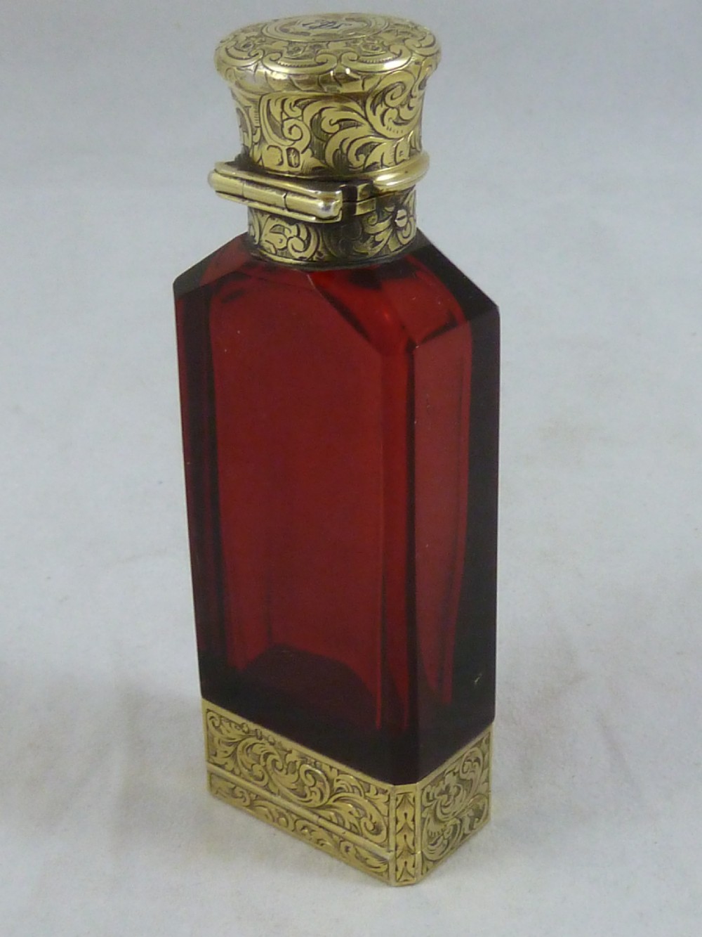 A faceted rectangular ruby red glass scent bottle featuring intricate scroll-engraved silver-gilt mounts at the cap and base. View IV