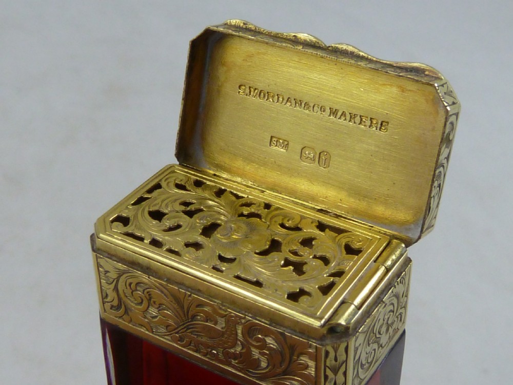 A faceted rectangular ruby red glass scent bottle featuring intricate scroll-engraved silver-gilt mounts at the cap and base. View V
