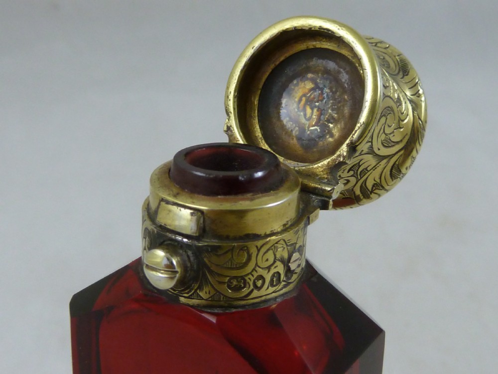 A faceted rectangular ruby red glass scent bottle featuring intricate scroll-engraved silver-gilt mounts at the cap and base. View IX