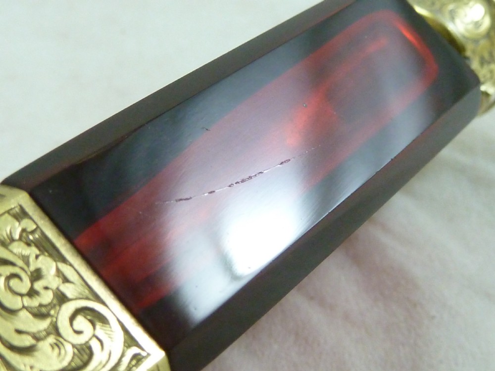 A faceted rectangular ruby red glass scent bottle featuring intricate scroll-engraved silver-gilt mounts at the cap and base. View X