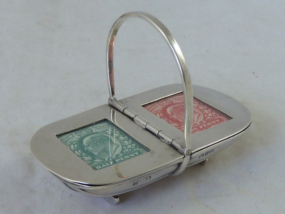 An Edwardian sterling silver double stamp case shaped like a garden trug with an overhead handle and two glazed stamp display compartments.