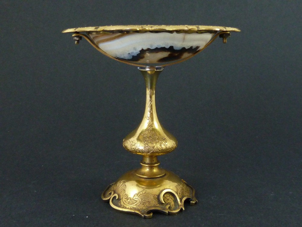 A miniature gilt brass tazza bowl featuring a central polished banded agate stone set within a chased Rococo scrollwork edge and pedestal foot. View II