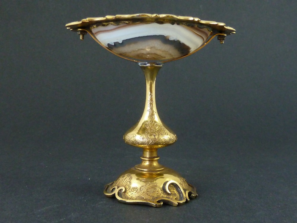 A miniature gilt brass tazza bowl featuring a central polished banded agate stone set within a chased Rococo scrollwork edge and pedestal foot. View V