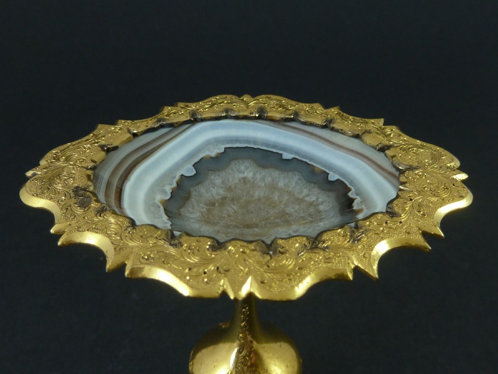 A miniature gilt brass tazza bowl featuring a central polished banded agate stone set within a chased Rococo scrollwork edge and pedestal foot. View VII