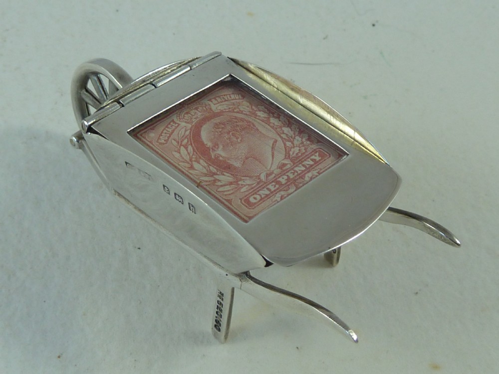 A miniature sterling silver stamp case shaped like a garden wheelbarrow with a clear glass window displaying a pink postage stamp. View III