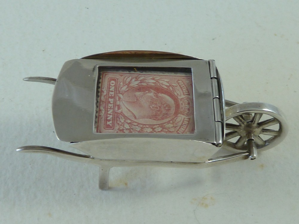 A miniature sterling silver stamp case shaped like a garden wheelbarrow with a clear glass window displaying a pink postage stamp. View VII